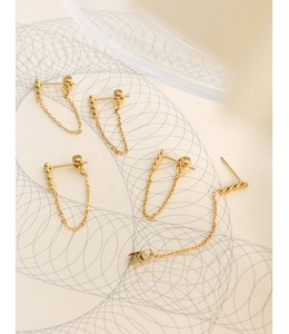Macro detail of gold geometric stud earrings with spiral texture and delicate chain fringes