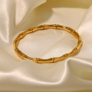 Détail d'un bracelet bambou en acier doré 18K sur un fond élégant en soie beige