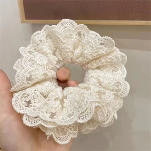 Detail of off-white lace scrunchie with floral embroidery pattern and soft mesh texture