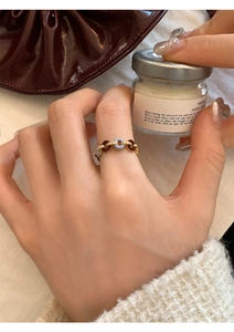 Detail of gold chain link ring with blue and brown enamel on hand with leather bag