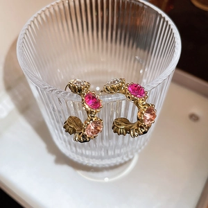 Detail of vintage C-shaped gold earrings with colorful rhinestones on a glass rim