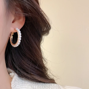 Close-up of elegant gold earrings with white pearls worn on a model's ear