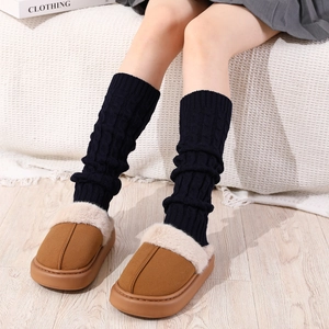 Close-up of brown faux suede winter slippers and thick black cable knit leg warmers