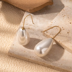 French vintage gold pearl drop earrings on beige travertine stone with soft shadows