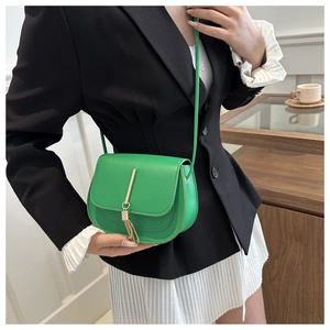 Close-up of vibrant green saddle bag with gold hardware tassel and slim shoulder strap