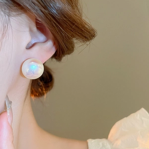 Close-up of an iridescent mermaid pearl stud earring worn on ear with blue luster