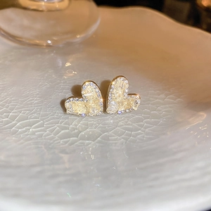 Close-up of heart-shaped gold stud earrings with yellow crystals and white micro-pave