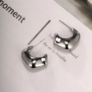 Macro shot of silver-colored C-shaped stainless steel earrings with polished organic texture