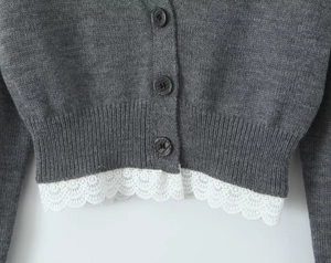 Détail d'un cardigan en maille gris foncé avec boutons et élégante bordure en dentelle blanche