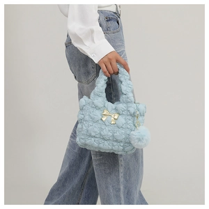 Detail of light blue quilted handbag with golden bow accent and plush pom-pom charm