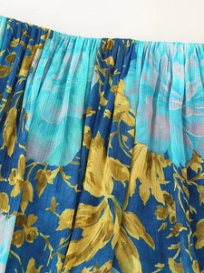 Close-up of pleated chiffon fabric with gold and blue floral patterns on dark blue dress