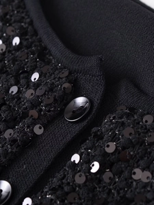 Dettaglio di paillettes nere e bottone in resina su giacca in maglia testurizzata da donna