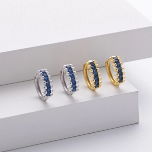 Detail of silver and gold spiked hoop earrings featuring blue square-cut gemstones