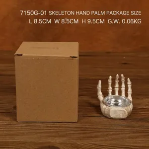 Detail of skull hand resin holder with antique finish next to its brown packaging box