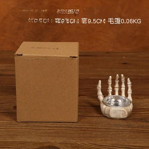 Detail of skull hand resin holder with antique finish next to its brown packaging box