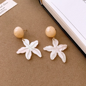 Detail view of starfish resin drop earrings in cream color on a vintage brown card