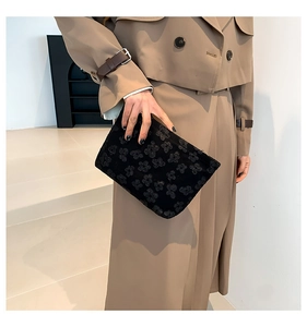 Close-up of black rectangular clutch featuring textured floral patterns and zipper detail