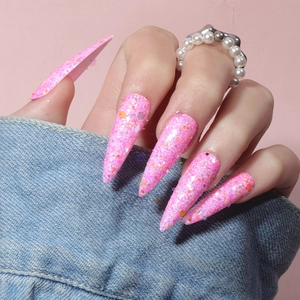 Close-up of long stiletto press-on nails with vibrant pink glitter and colorful sequins