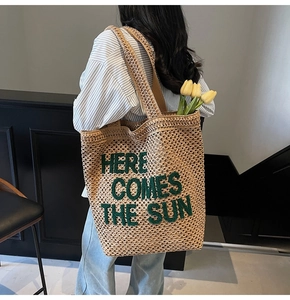 Detail of straw tote bag with green 'HERE COMES THE SUN' embroidery on back of model