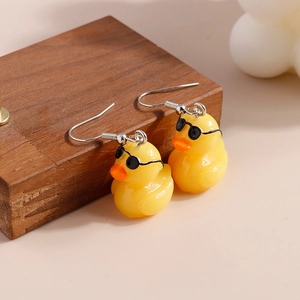 Close-up of cute yellow duck earrings with black sunglasses on a wooden block