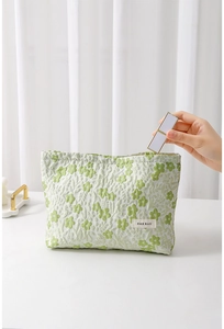 Detail of floral makeup bag in green jacquard fabric with lipstick being placed inside