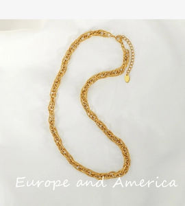 Detail of gold intertwined link chain necklace featuring a small metal drop tag on fabric