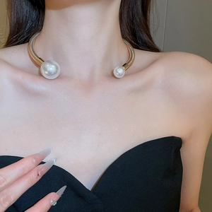 Close-up of a gold open collar necklace with two large white pearls worn by a female model