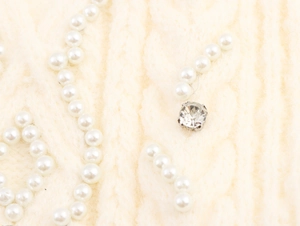 Detailed macro view of elegant white pearls and a crystal rhinestone on knit fabric