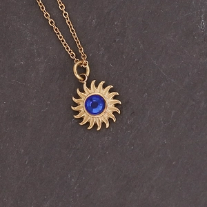 Detailed close-up of golden sunflower pendant necklace with blue gemstone on stone background