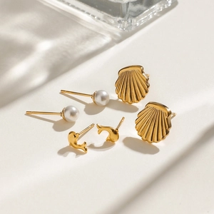 Détail de trois paires de boucles d'oreilles en acier avec motifs coquillage, dauphin et perle
