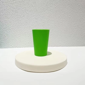 Detail of a solid green plastic stacking cup displayed on a minimalist white pedestal stand