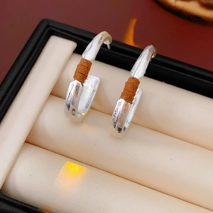 Macro view of matte silver C-shaped earrings with brown leather wrap on jewelry box