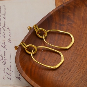 Detailed shot of interlocking oval gold earrings on a vintage wooden tray background