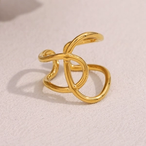 Detailed view of the 18K gold plated knotted crisscross open ring on a textured surface