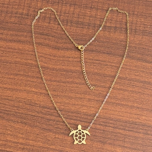 Détail d'un pendentif tortue ajouré sur une chaîne dorée sur une surface en bois