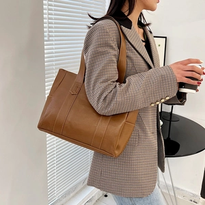 Brown large capacity PU leather tote bag worn by a model in a stylish office setting