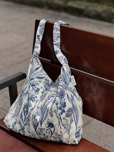 Artistic tie-dye style canvas tote bag with blue floral pattern on a wooden bench