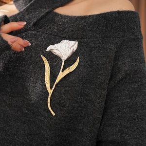 Close-up of a tulip brooch with silver petals and golden stem on a grey sweater