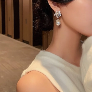Close-up of golden snowflake earrings with zircon crystals and a hanging white pearl