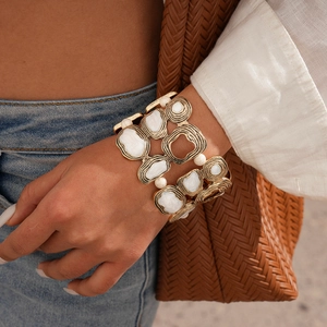 Detailed view of wide gold geometric bracelet with white marble stone worn on wrist