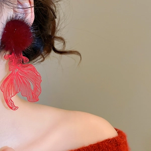 Detail of red hollow fish earrings with plush pompom on a model in close-up shot