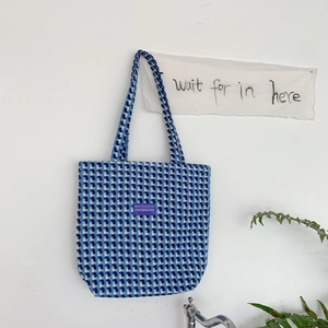 Detail of blue and white plaid woven tote bag with a small purple logo label