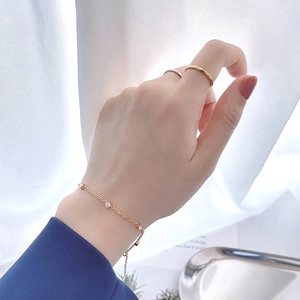 Bracelet en titane doré avec zircons et bagues minimalistes portés sur un plateau inox