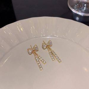 Detail of elegant gold-tone bow earrings with sparkling rhinestone tassels on ceramic tray