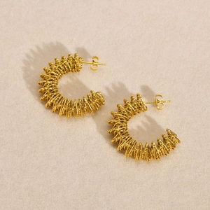 Detailed close-up of golden spiral twisted hoop earrings on a neutral beige background