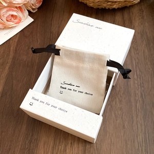 Beige canvas drawstring pouch and white paper jewelry gift box set on a wooden table