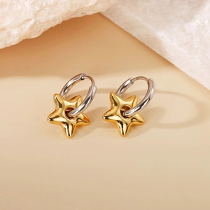 Detail view of two-tone gold star pendant earrings on white mineral stone texture