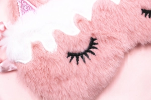 Detailed close-up of pink plush unicorn sleep mask with embroidered eyes and glittery ears