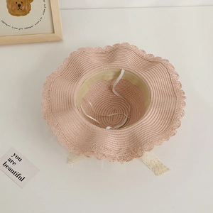 Détail d'un chapeau de paille rose avec bord ondulé, mentonnière et rubans en dentelle