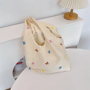 Detailed embroidery of colorful bow patterns on a beige canvas tote shoulder bag
